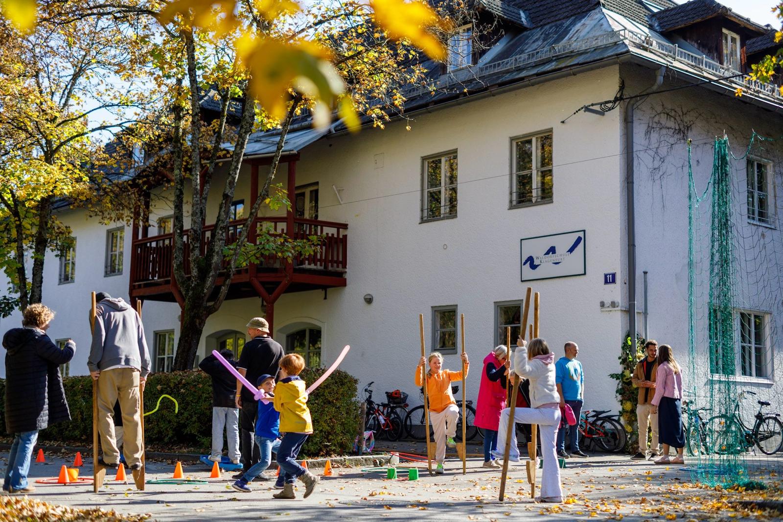 Ansicht des Schulgebäudes im Herbst mit spielenden Kindern davor.